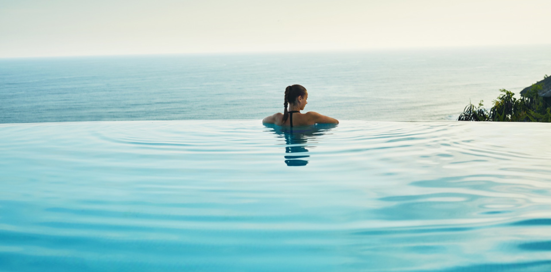 femme acoudée au bord de sa piscine regarde la mer