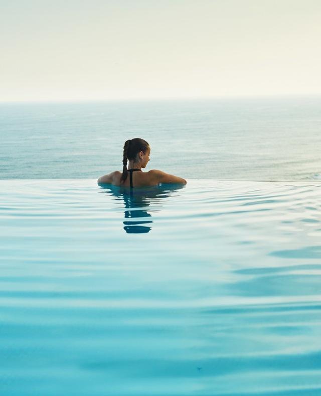 femme accoudée au bord de sa piscine regarde la mer